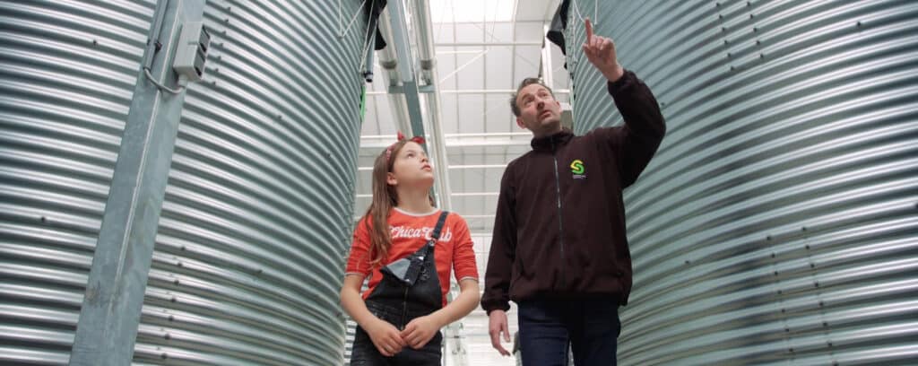 Man and girl walking through greenhouse with water reservoir behind them