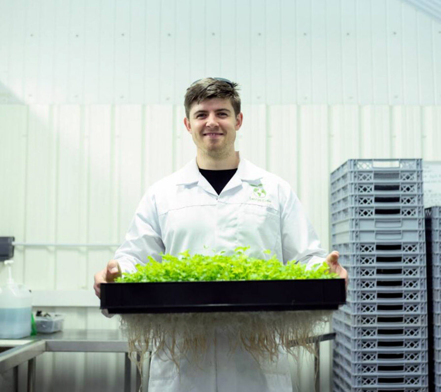 Man wearing lab coat holding up tray with plants