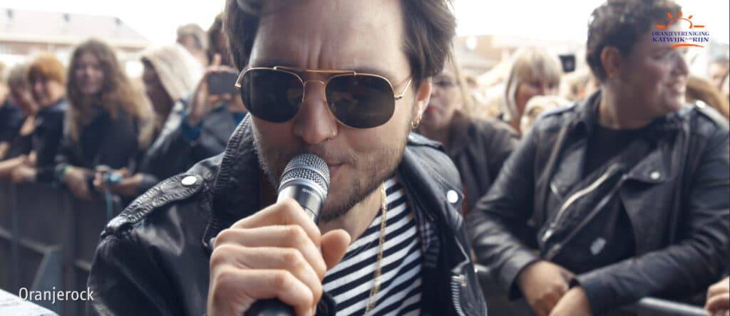 Man singing into microphone looking at camera with crowd behind him