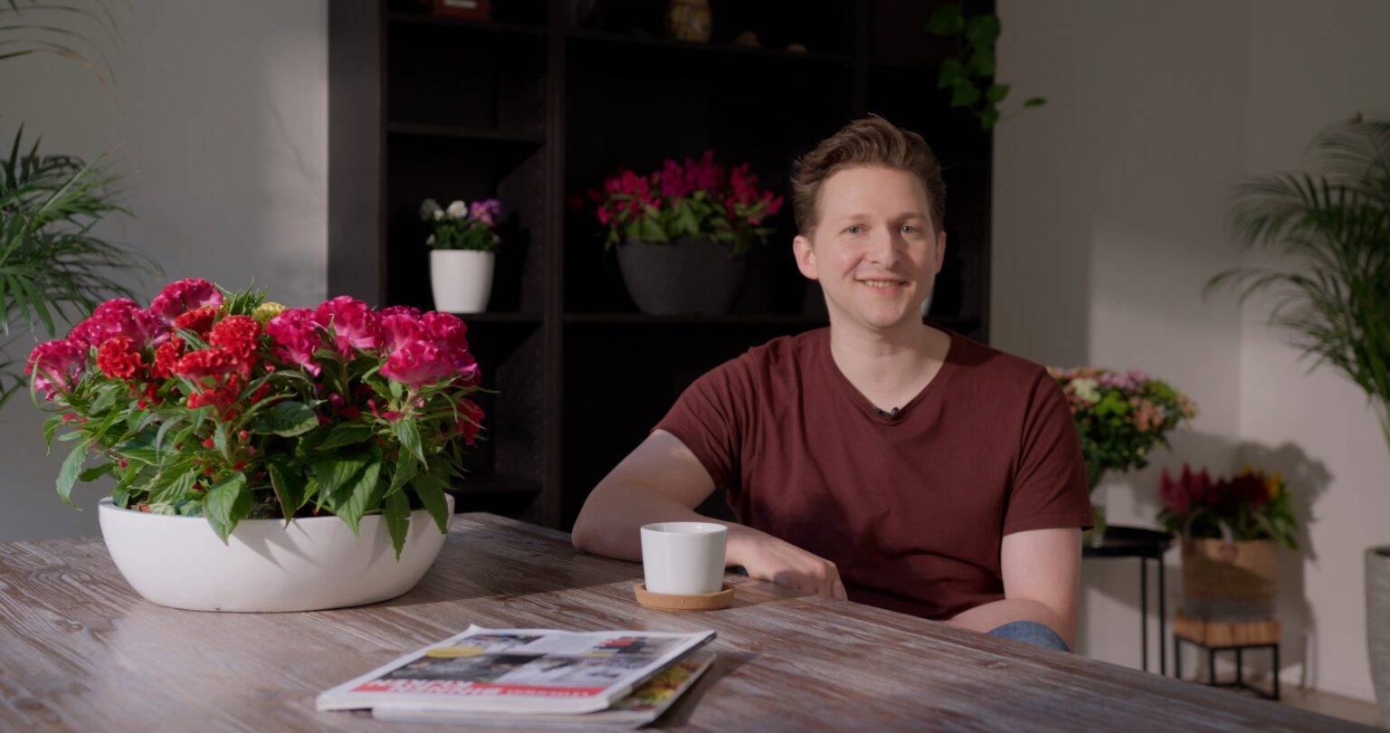 Man sits in chair with flowers smiling - Floritec bedrijfsfilm presentator - behorend bij blog de mogelijkheden van video