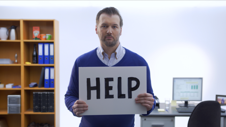 Man standing in office setting holding help sign